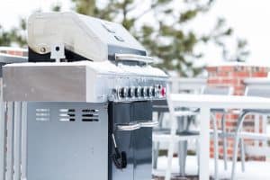 Seitenansicht eines geschlossenen Gasgrills, der mit Schnee bedeckt ist