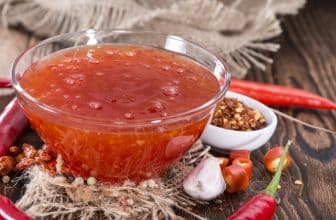 Glasschale mit Chilisauce auf Holztisch neben Kräutern und Gewürzen