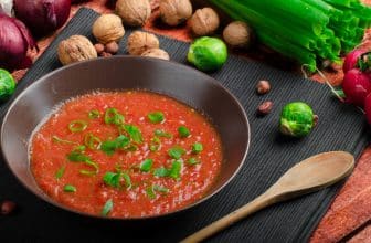 Scharfe rote Sauce in schwarzer Schale, daneben Holzlöffel und Walnüsse