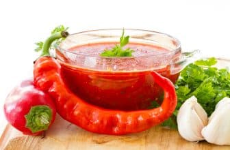 Frische rote Chilischote vor mit rotr Sauce gefülltem Glasschälchen