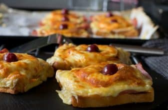 Mehrere Toast Hawaii auf Küchentisch, im Hintergrund mit Toast Hawaii gefülltes Backblech
