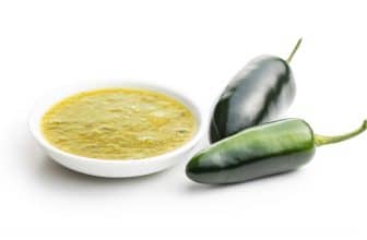 Grüne Jalapeno Chillis neben weißem Schälchen mit Sauce