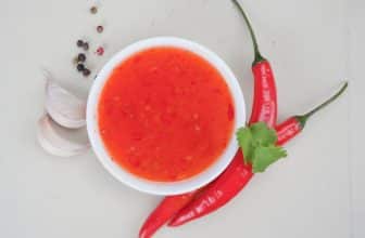 Rote Chilisauce vor hölzernem Hintergrund in weißem Schälchen