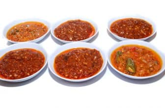 Sechs verschiedene Chilisaucen in weißen Schälchen